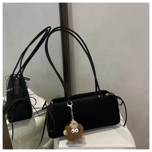 Close-up of black plush underarm bag with ribbon bow and cute monster pendant detail
