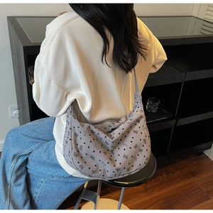 Grey corduroy hobo bag with heart and bow patterns worn by a model in a casual setting