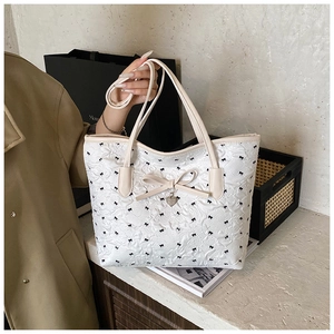 Détail du sac fourre-tout matelassé crème avec imprimés nœuds noirs et breloque en cœur