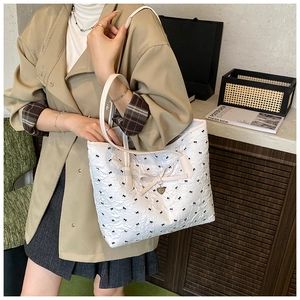 Détail du sac cabas blanc avec motifs nœuds noirs et pendentif en métal en forme de cœur