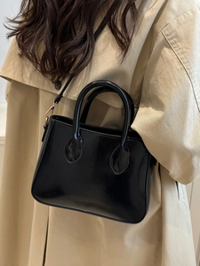 Glossy black retro top-handle crossbody bag with golden hardware on a beige coat model
