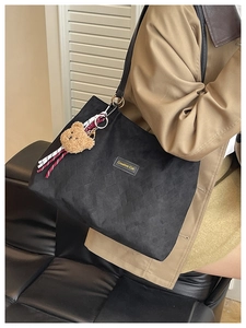 Détail d'un grand sac fourre-tout noir avec texture matelassée et breloque ours peluche