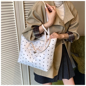 Détail d'un sac cabas blanc avec imprimé nœuds noirs et breloque cœur sur mannequin