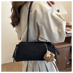 Close-up of black fuzzy shoulder bag with cute monster plush charm on trench coat