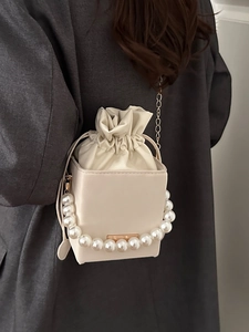 Cream square bucket bag with pearl handle and drawstring pouch shown on a model