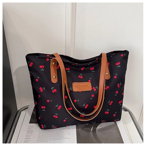 Detailaufnahme der schwarzen Tragetasche mit Kirschmuster und braunen Ledergriffen
