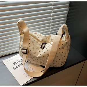 Detail of cream corduroy crossbody bag featuring brown heart patterns and double zippers