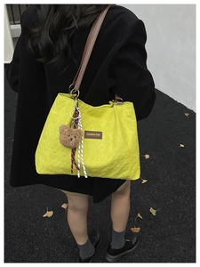 Détail du cabas matelassé jaune avec lanières en cuir marron et accessoire pendentif ours