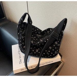 Detail of black corduroy crossbody bag featuring white bow patterns and dual zippers