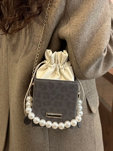 Chic leopard print bucket bag with large pearl trim and golden chain strap on brown coat