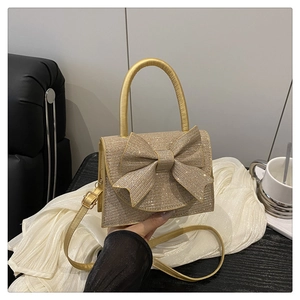 Dettaglio borsa da sera dorata con strass, fiocco decorativo e manico con cristalli
