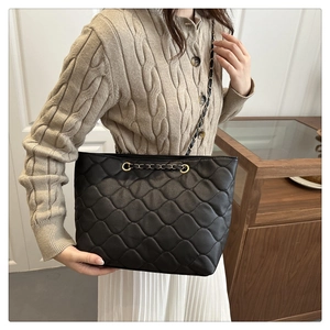 Close-up of black quilted tote bag with metallic chain and faux leather texture