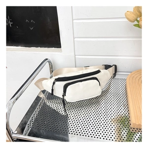 Detail view of cream oxford cloth waist bag with black zippers on a metal rack