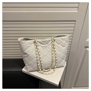 Detail of white quilted tote bag with golden chain straps and soft rhombic texture