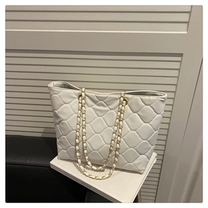 Detail of white quilted tote bag with golden metal chain strap and soft leather texture