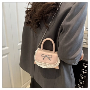Dettaglio mini borsa rosa con fiocco argento e pizzo bianco su blazer grigio