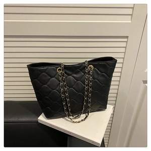 Detail view of black quilted tote bag with gold chain strap on white book prop
