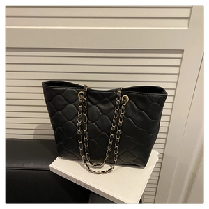 Detail of black quilted tote bag with large diamond stitching and gold chain strap