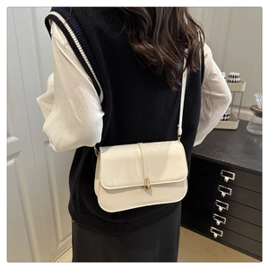 Detail of a minimalist cream baguette bag with a gold twist lock and smooth PU texture