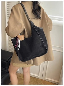 Detail of a large black suede tote bag with bear charm shown from a side view on a model
