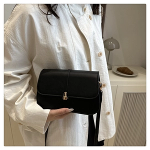 Detail of minimalist black baguette bag with gold hardware buckle and matte leather texture