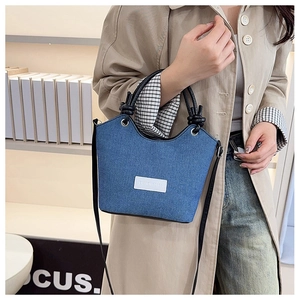 Détail du sac seau en jean avec poignée tressée porté par un mannequin chic
