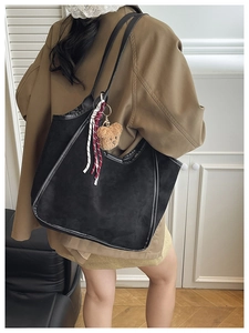 Detail view of black suede hobo shoulder bag with plush bear charm and striped rope decor