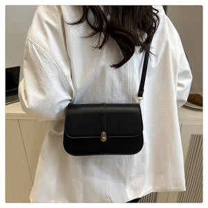 Detail of a minimalist black leather baguette bag with a gold metal clasp on a model