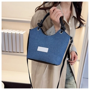 Détail du sac seau en denim avec poignée nouée et étiquette de mode en cuir blanc