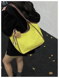 Detail of yellow suede shoulder bag with brown leather trim and cute bear charm