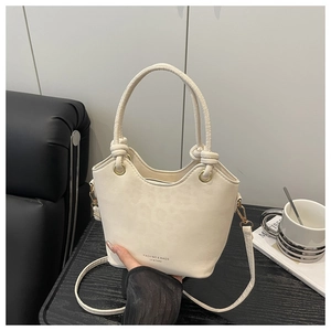 Macro shot of cream bucket bag detail with unique knotted handle and gold hardware
