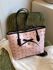 Sac fourre-tout rose avec nœuds noirs et pendentif en cœur sur une chaise verte