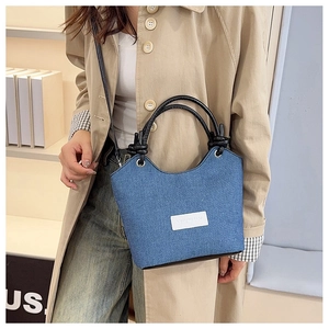 Détail d'un sac seau en denim bleu avec poignée nouée en cuir noir et patch logo
