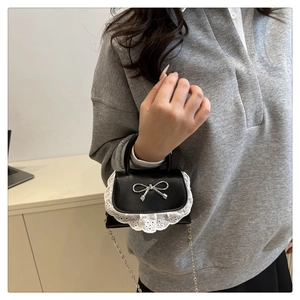 Dettaglio mini borsa in pelle nera con bordo in pizzo e fibbia a fiocco argento
