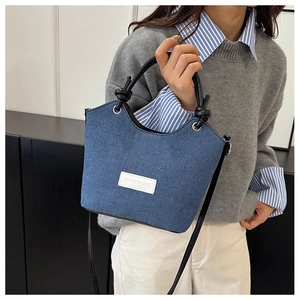 Sac seau en denim avec écusson logo blanc et poignées en cuir noir porté par un mannequin