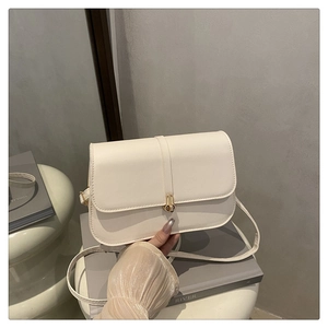 Detail shot of a minimalist cream baguette bag with elegant golden U-shaped metal buckle lock