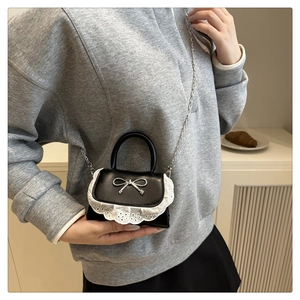 Dettaglio mini borsa nera con bordo in pizzo bianco e fiocco in metallo argento