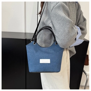 Détail du sac seau en jean bleu avec base en cuir noir et étiquette de mode