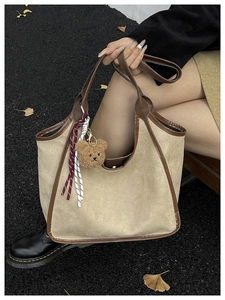 Detailed close-up of beige suede tote bag with brown leather handles and bear pendant