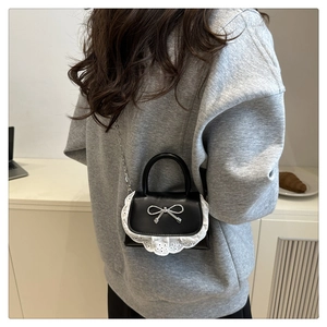 Dettaglio mini borsa nera in pelle con bordo in pizzo bianco e fiocco in metallo argento