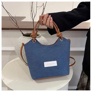 Détail du sac seau en denim avec poignées en similicuir marron et écusson logo