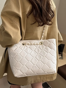 Large white quilted tote bag with gold chain strap worn by a model in casual style
