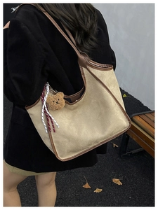 Detail of beige suede tote bag with brown leather trim and plush bear charm accent