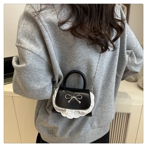 Dettaglio di mini borsa nera in ecopelle con fiocco argentato e bordo in pizzo bianco