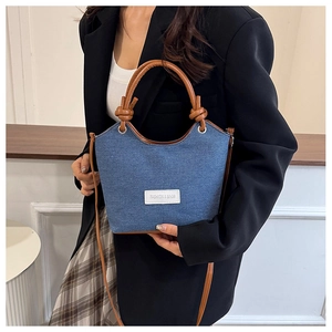 Détail du sac seau en jean montrant l'anse en cuir marron avec un décor de nœud élégant