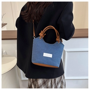 Sac seau en denim bleu avec anses en cuir marron porté par un mannequin chic