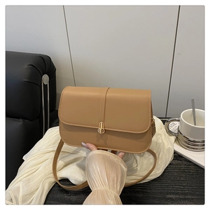 Detail of light brown baguette bag with gold round metal clasp on silk fabric