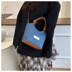 Détail d'un sac seau en denim avec poignées en cuir marron et design décoratif à nœud