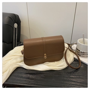 Detail of coffee brown baguette bag with golden capsule lock on black wooden table