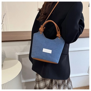 Détail du sac seau en denim bleu avec poignée en cuir marron nouée et écusson blanc